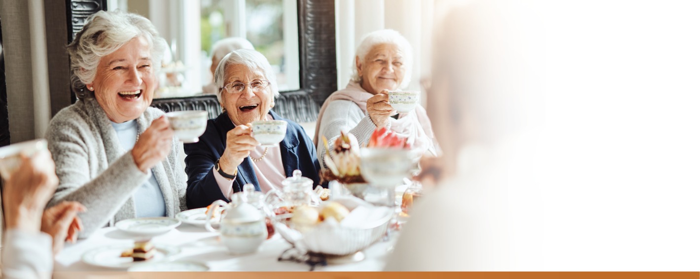 Three senior women lifting their tea cups in a toast and laughing.